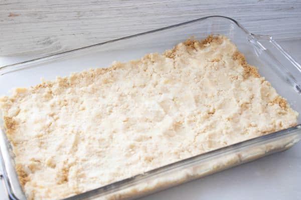 graham cracker crumbs in a glass baking dish topped with a crumble mixture on a white counter