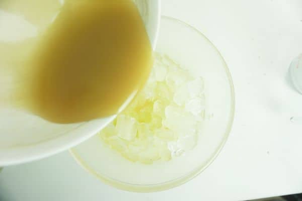 caramel sauce being poured into ice in a glass bowl on a white background