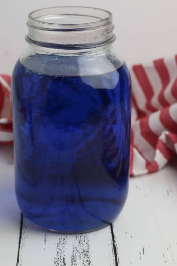 lime juice dyed blue in a glass jar a glass jar next to a red and white striped cloth on a white wood table