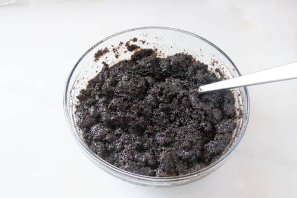crushed oreos and melted butter mixed together by a spoon in a glass bowl on a white counter