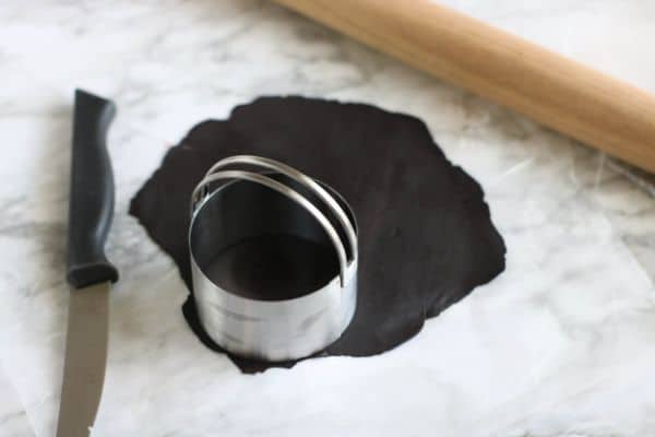 black fondant with a circle cookie cutter on it next to a knife on a gray counter