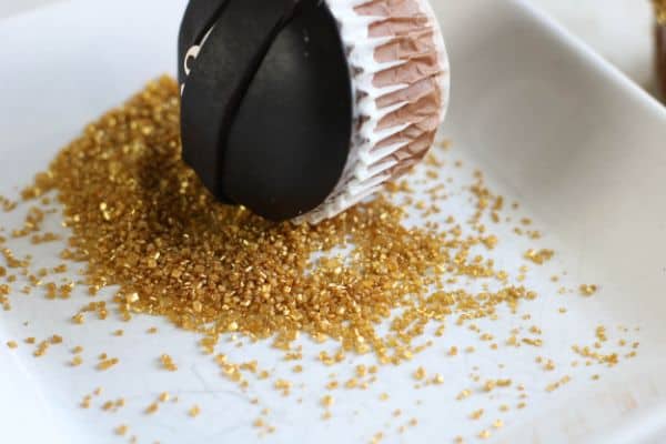 a ninja cupcake getting rolled in gold sugar sprinkles in a white dish