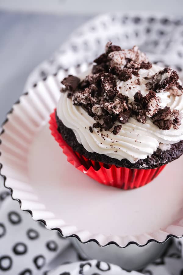 closeup of cookies and cream cupcake on a white pedestal on a black and white cloth 