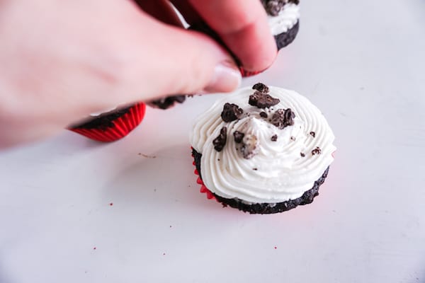 a hand sprinkling cookie pieces on a cupcake