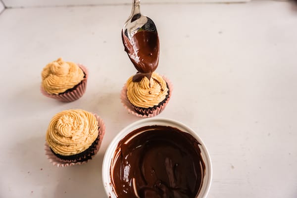 chocolate being drizzled onto a frosted cupcake