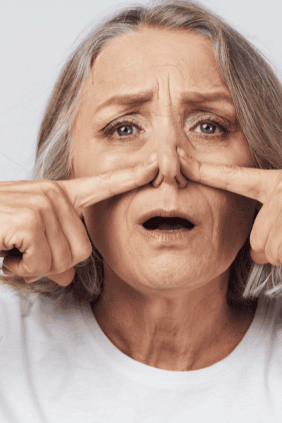 An older woman pinching her nose with her fingers.