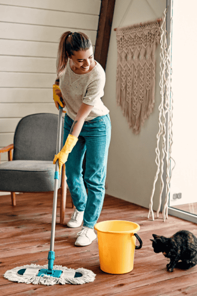 An image of a woman mopping the floor with a black cat on the side.